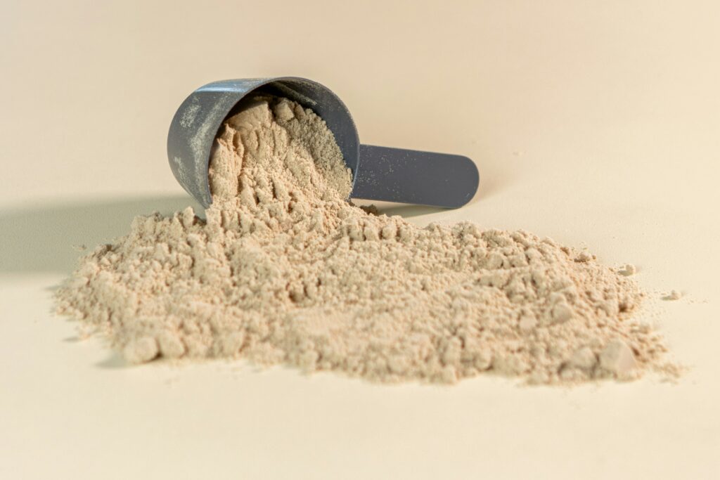 White protein powder spilling from scoop onto a tan surface.