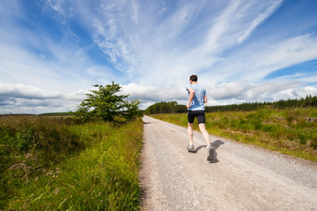 Man running down a dirt trail outside on a sunny day